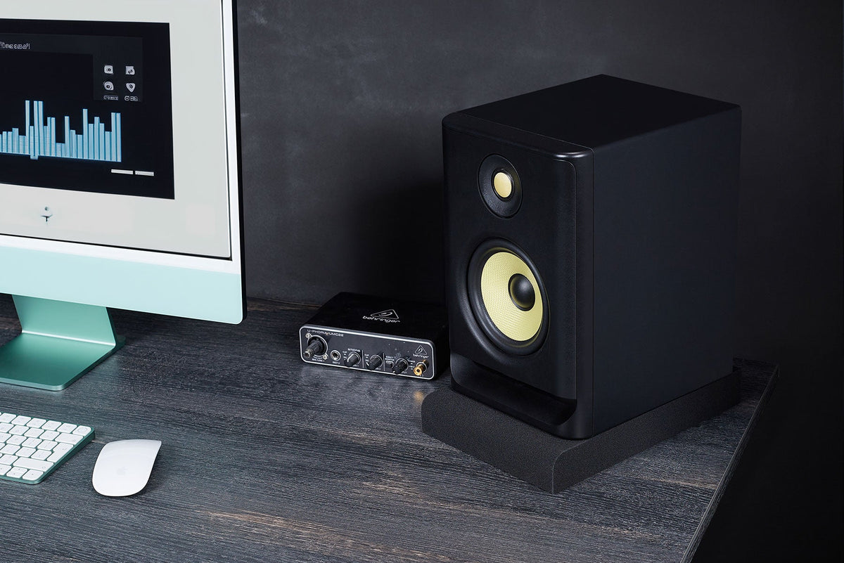 Studio monitor with a yellow woofer on an SMPad 5 isolation pad on a desk
